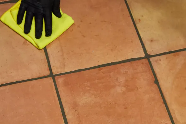 A gloved hand wiping a terracotta tile floor with a cloth