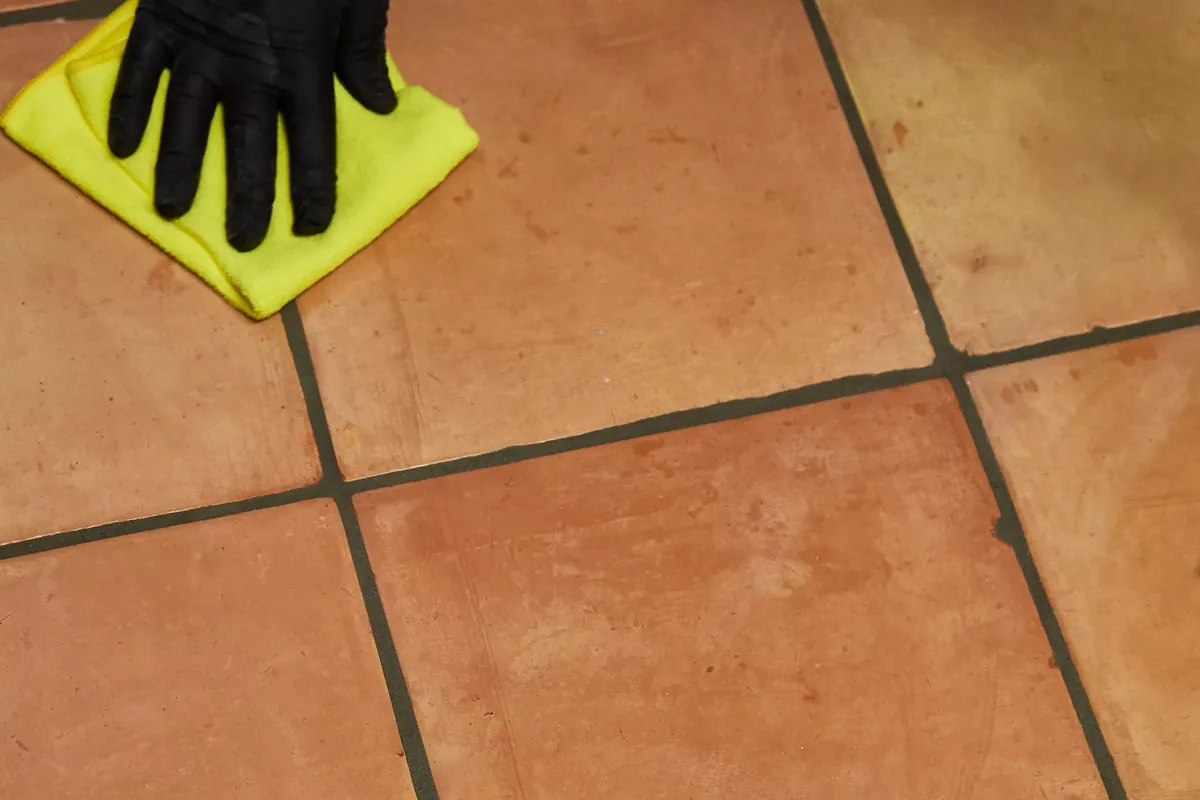 A gloved hand wiping a terracotta tile floor with a cloth
