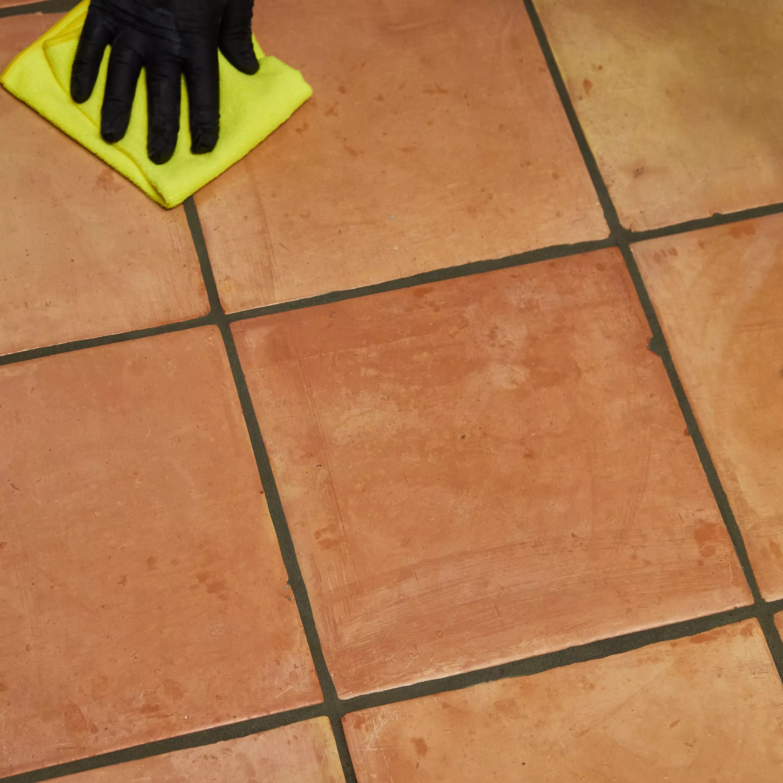 Terracotta tile floor and grout lines being cleaned with a cloth
